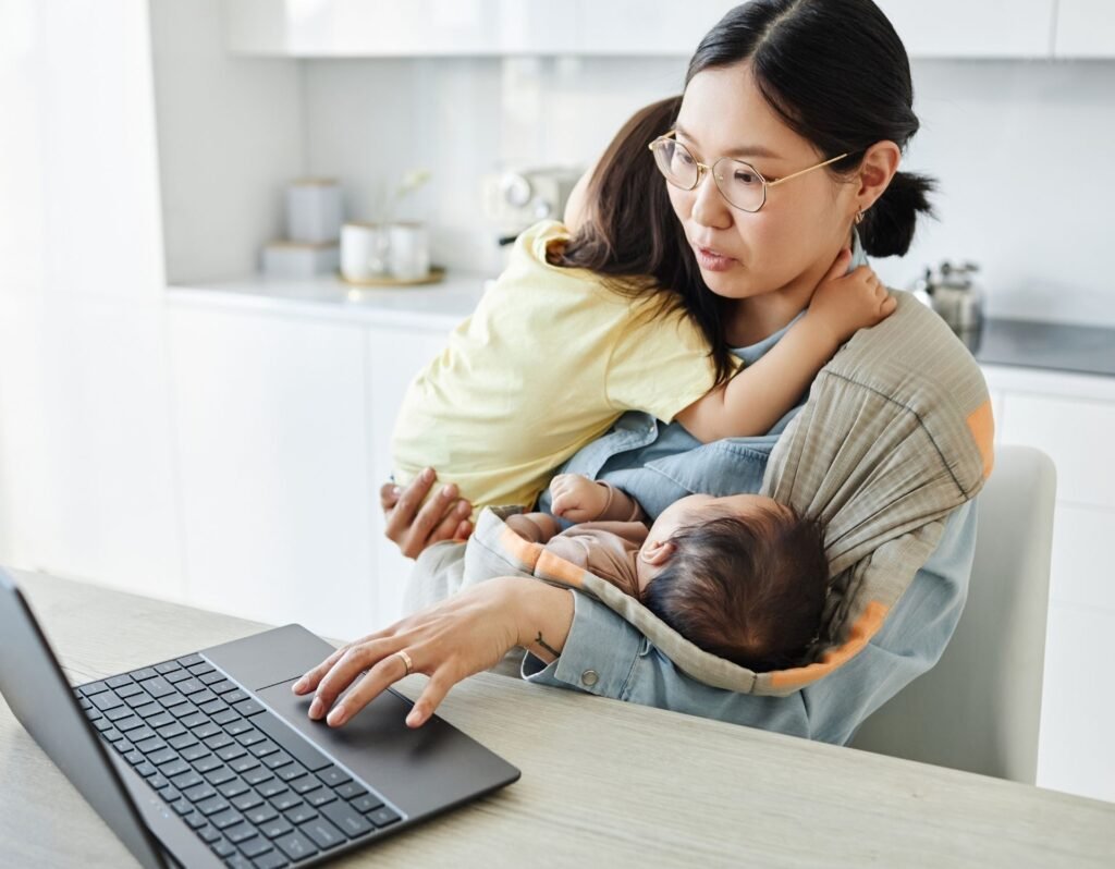 Stay at home mom working a side hustle on the computer holding two children