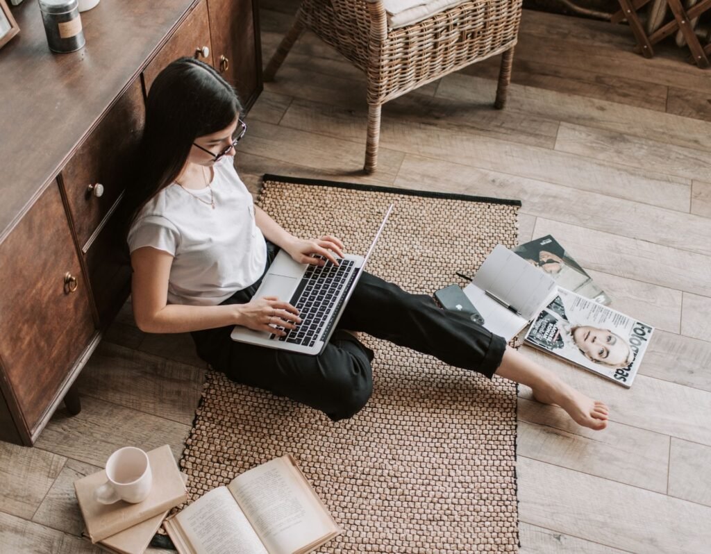 woman sitting on the floor surrounded by blog articles and magazines, working on her laptop