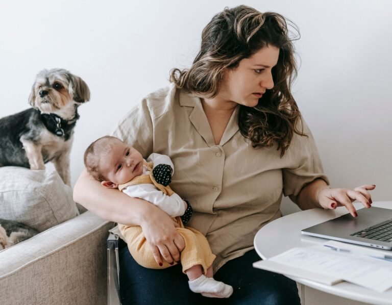 mom working side hustle from home. Working while holding a baby working on the laptop writing blogs for a side hustle