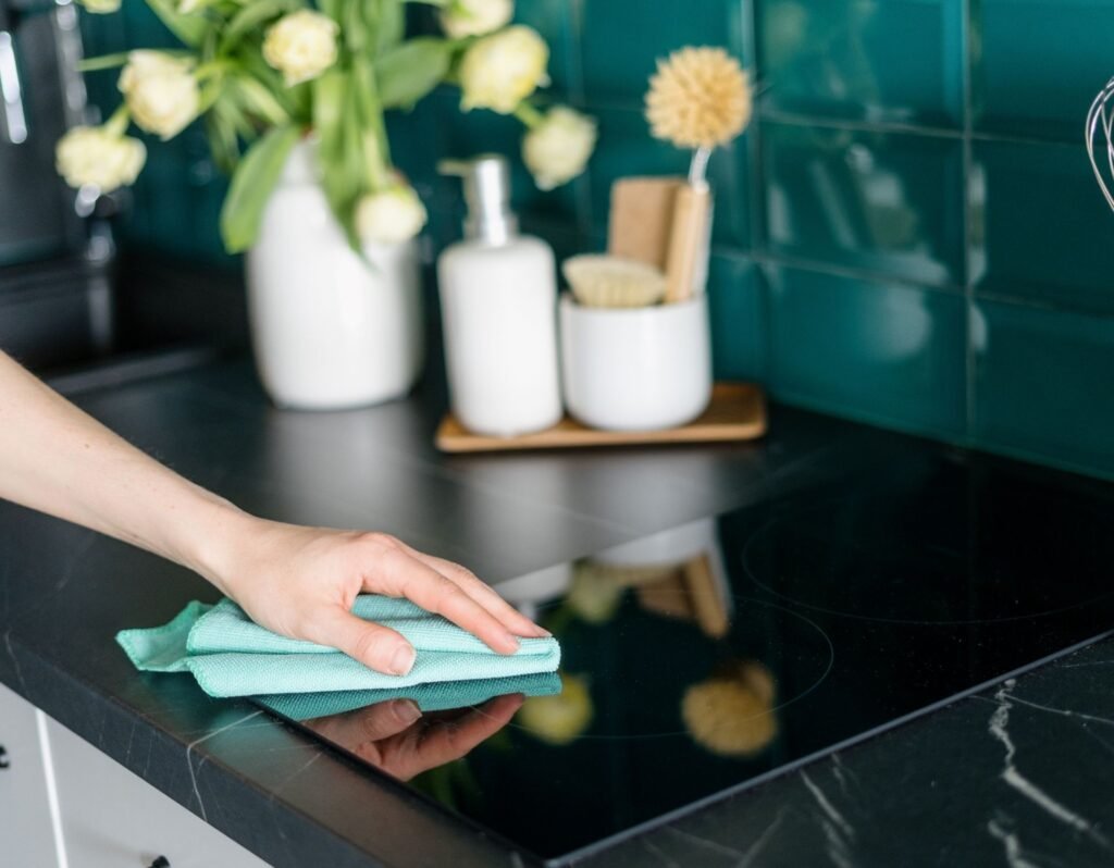 hand in frame holding a microfiber towel cleaning a glass stove top