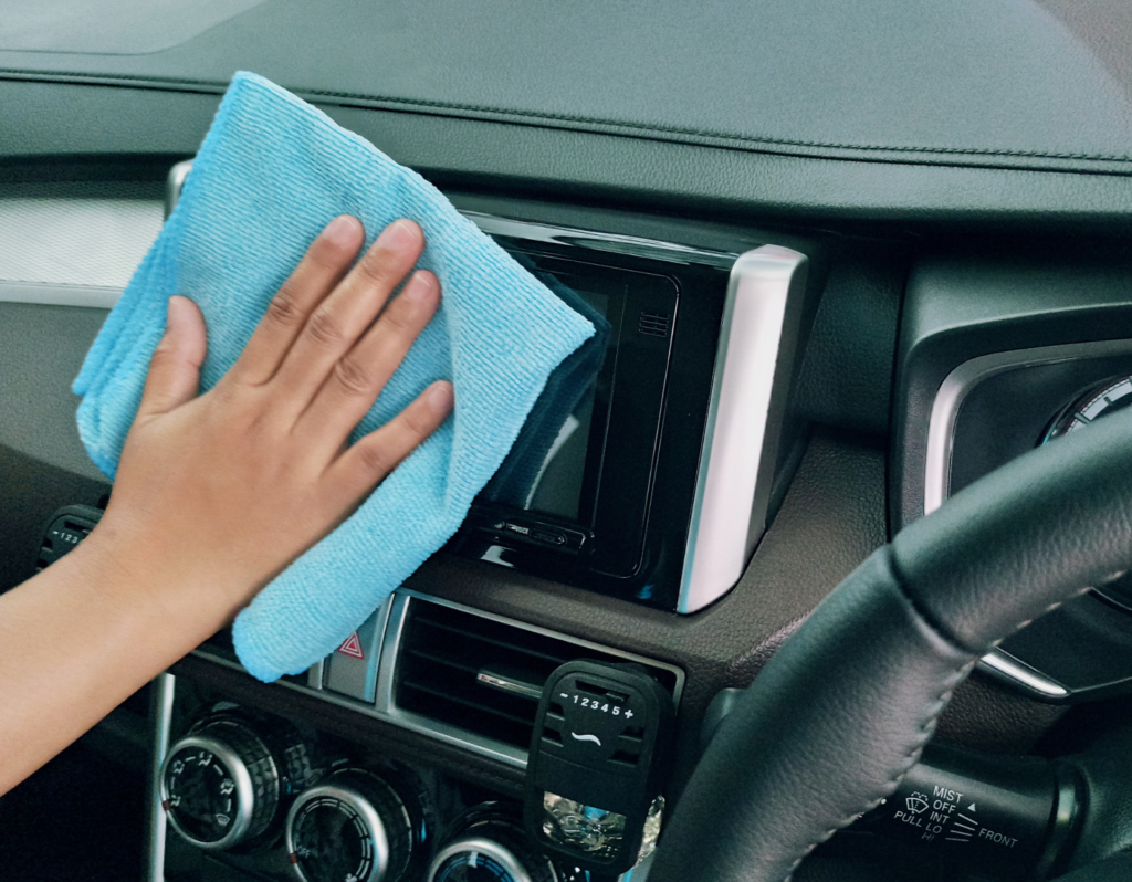 hand holding a microfiber towel and cleaning the screen on the dashboard of their car.