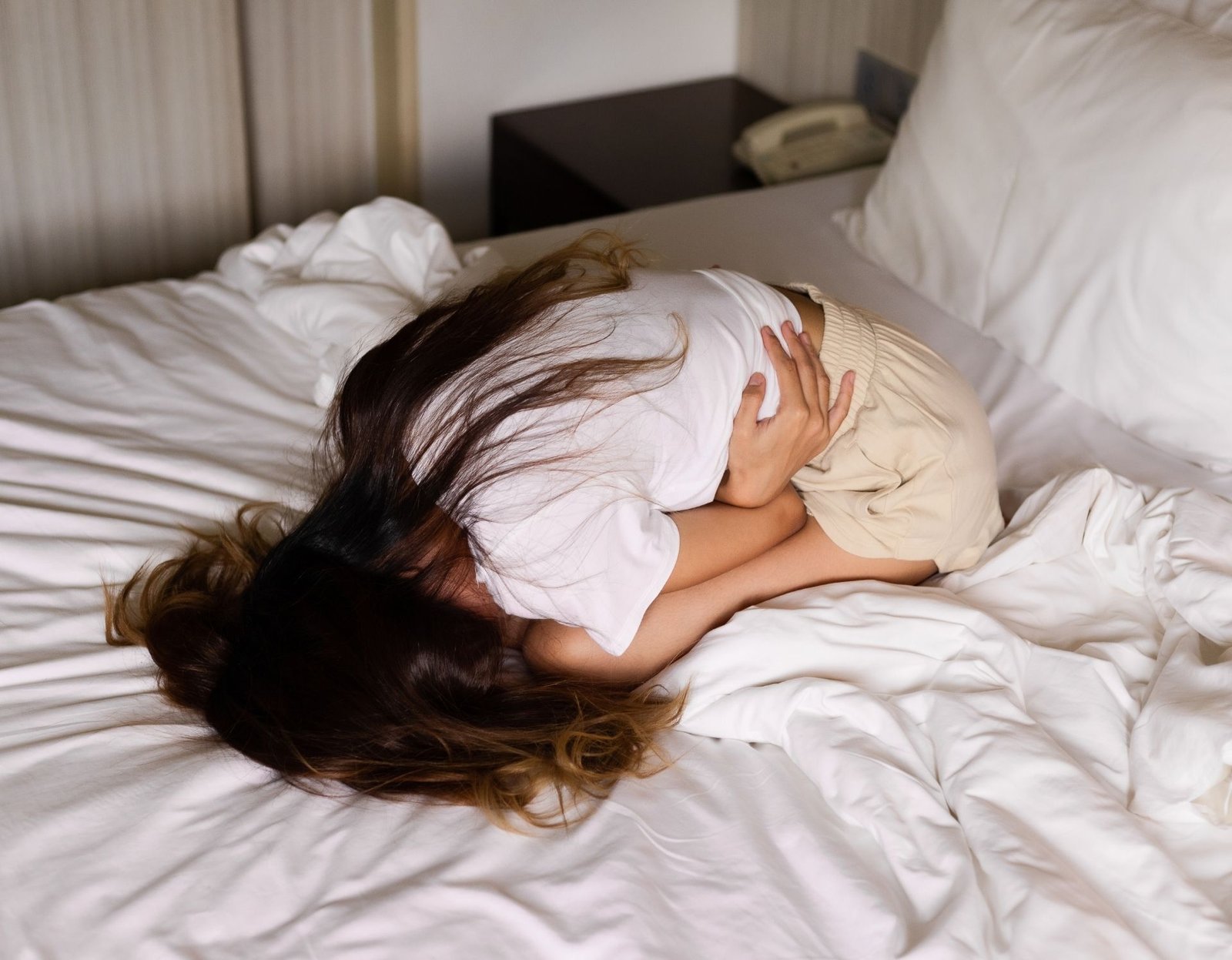 woman in pain in bed, curled up in a ball