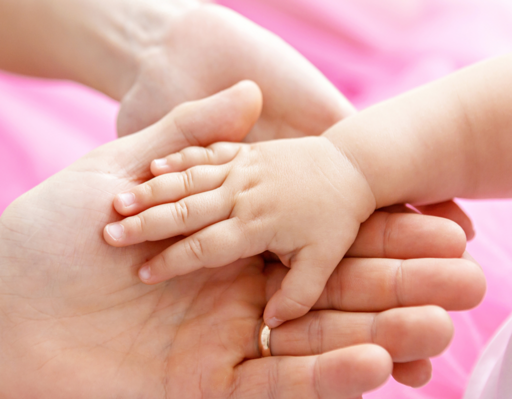 mom and baby girl holding hands with pink background