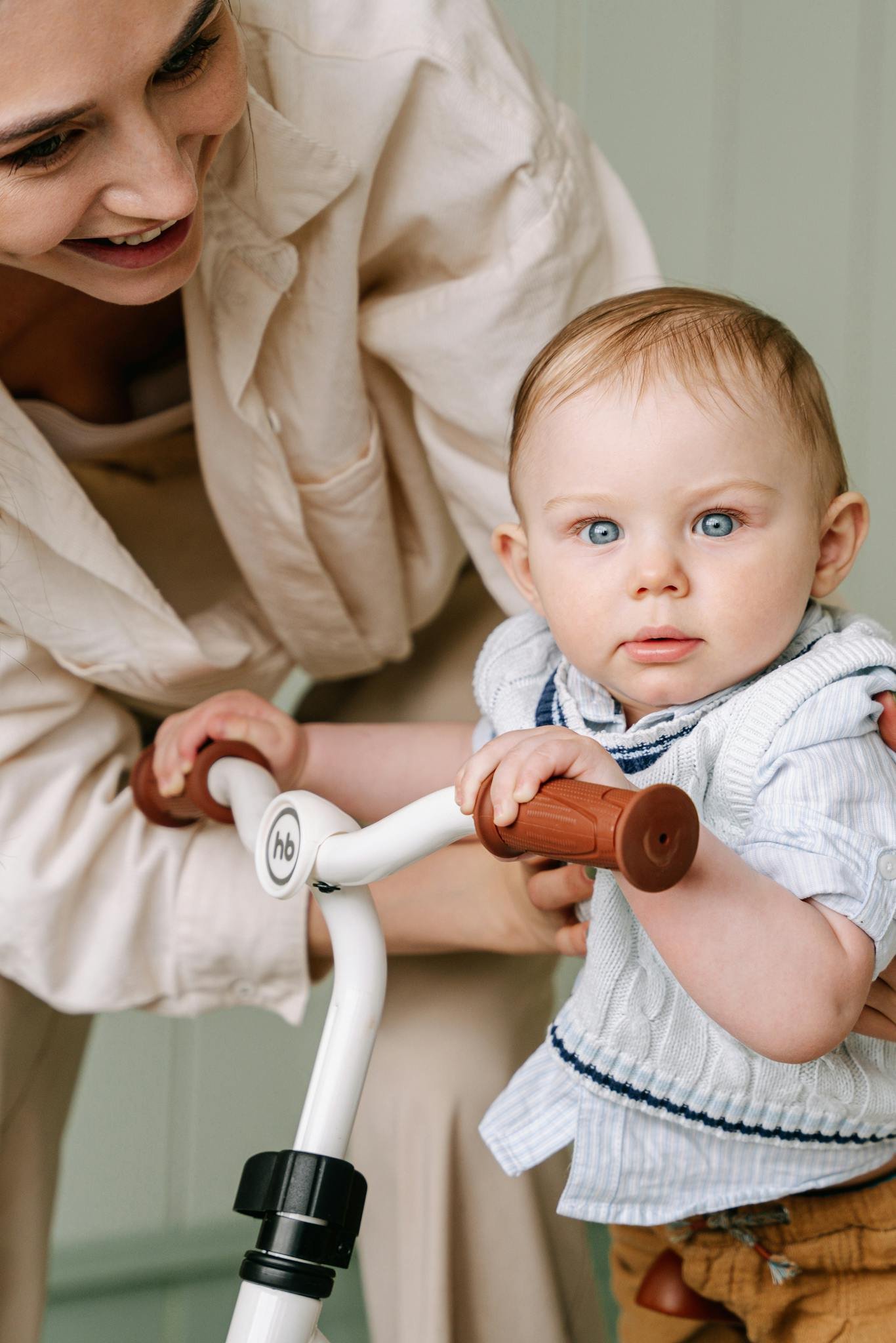 A mother helps her baby learn to ride a bicycle indoors. Heartwarming family moment.